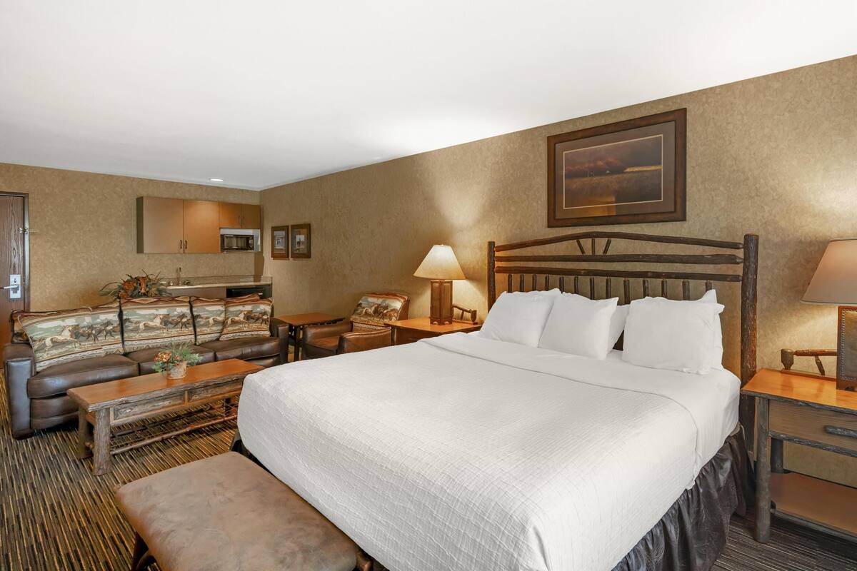 A hotel room with a large bed, a sofa, a small table, a lamp, and a picture on the wall.