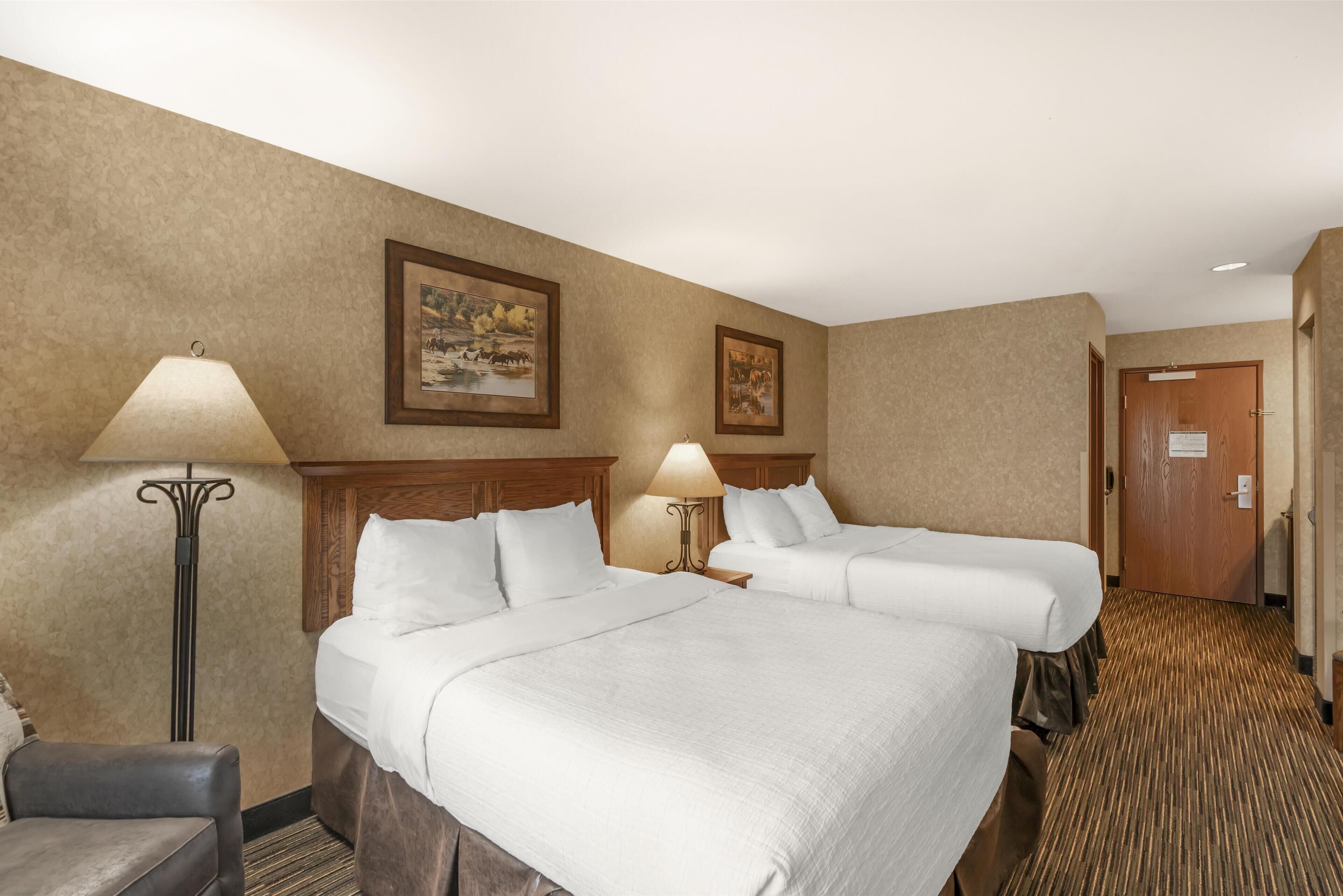 A hotel room with two beds, a chair, a lamp, and framed pictures on the wall.