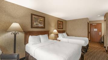 Quarto de hotel com duas camas, uma cadeira, um abajur e quadros nas paredes.