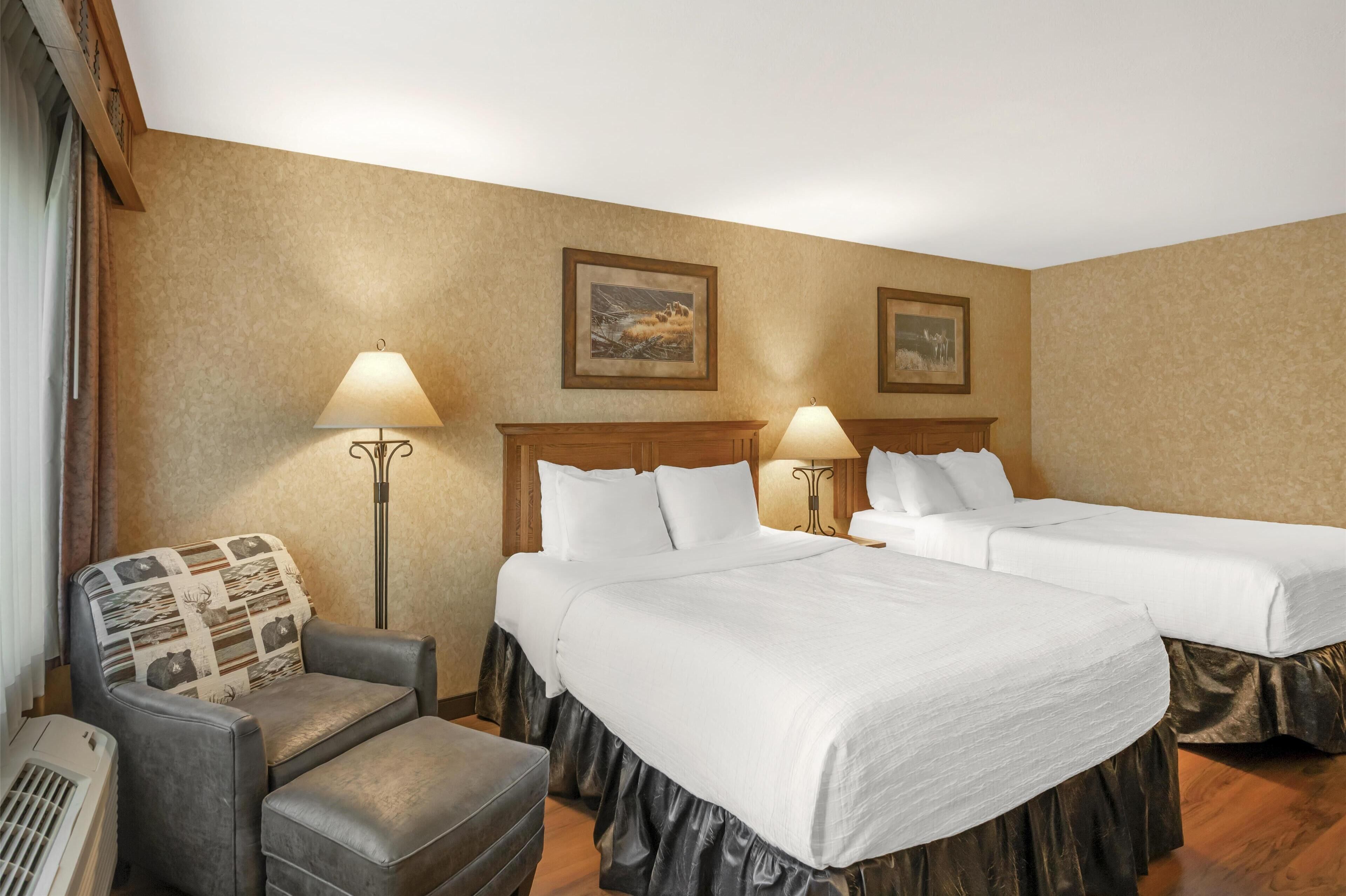 A hotel room with two beds, a chair, a lamp, and a picture on the wall.