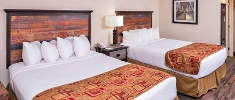 A hotel room with two beds, a nightstand with a lamp, a framed picture on the wall, and a carpeted floor.