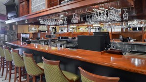 A bar area with a long counter, multiple stools, and hanging glassware.