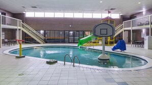 An indoor swimming pool with a slide, a basketball hoop, and a covered seating area.