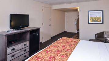 Una habitación de hotel con una cama, televisión, escritorio con cajones, silla y puerta que da a otra habitación.