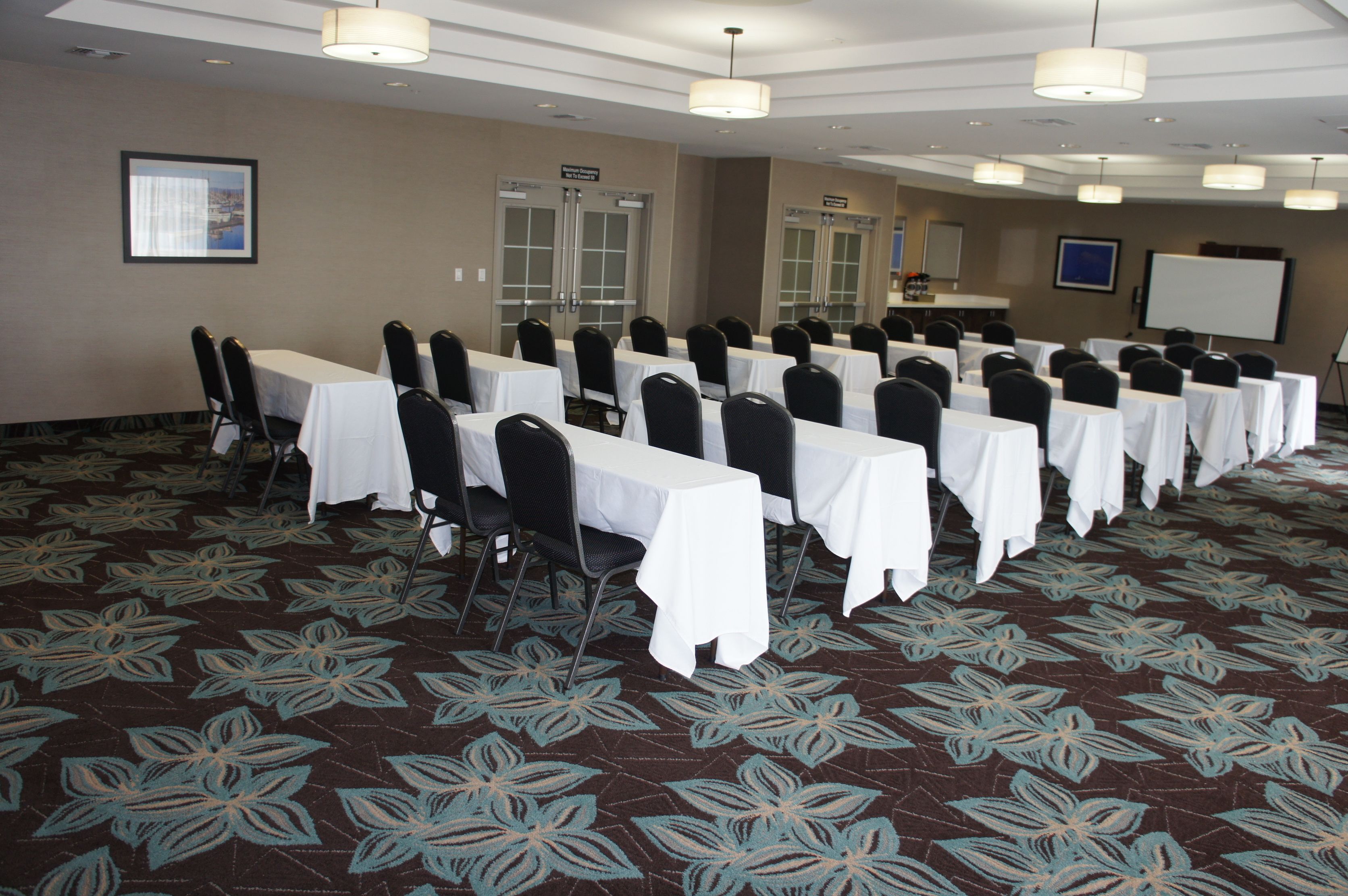 A conference room with rows of tables and chairs, a whiteboard, and a carpeted floor.