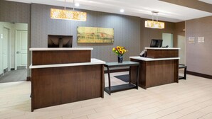 Un espace d’accueil comprenant deux comptoirs de réception en bois, un tableau accroché au mur et un vase rempli de fleurs placé sur le comptoir central.