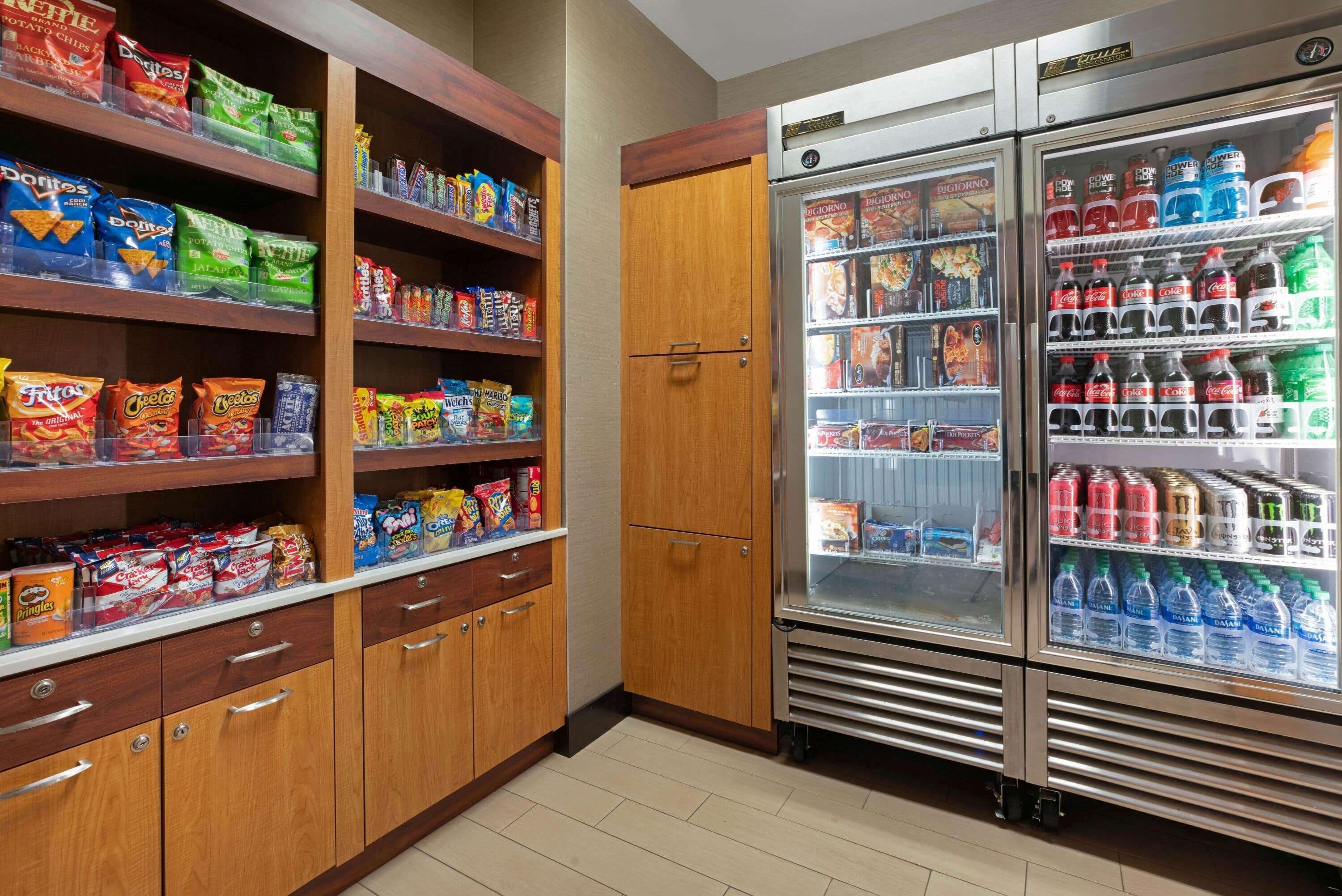 A snack and beverage area with shelves stocked with chips, snacks, and a refrigerator containing various drinks.