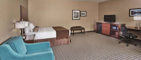 A hotel room with a bed, a desk with a computer, a TV, a chair, and a sofa.