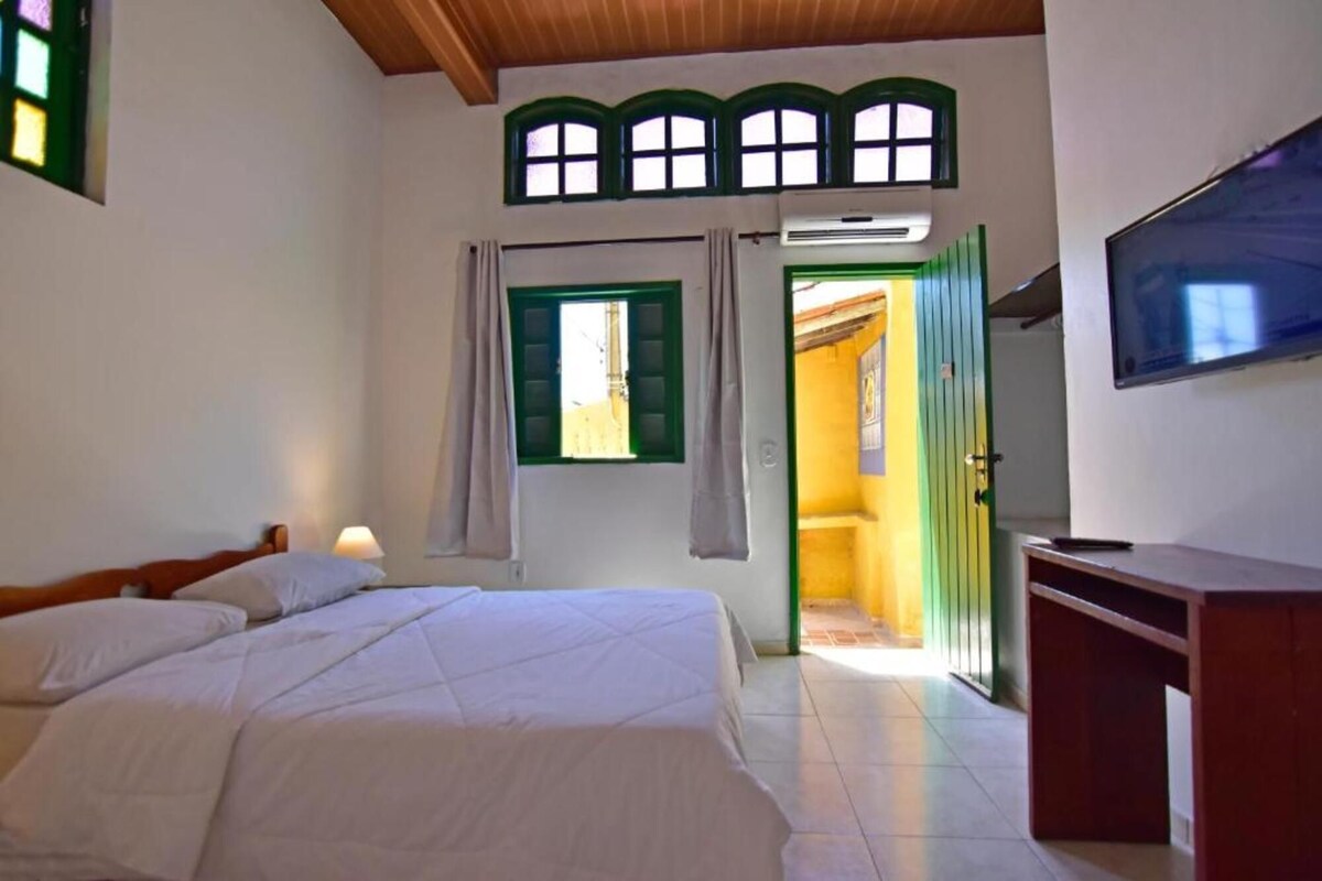A bedroom with a bed, a desk, a television, and a window with curtains.
