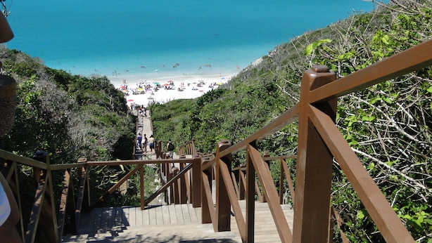 Una escalera de madera que lleva a una playa con agua azul cristalina y vistas de la playa de abajo.