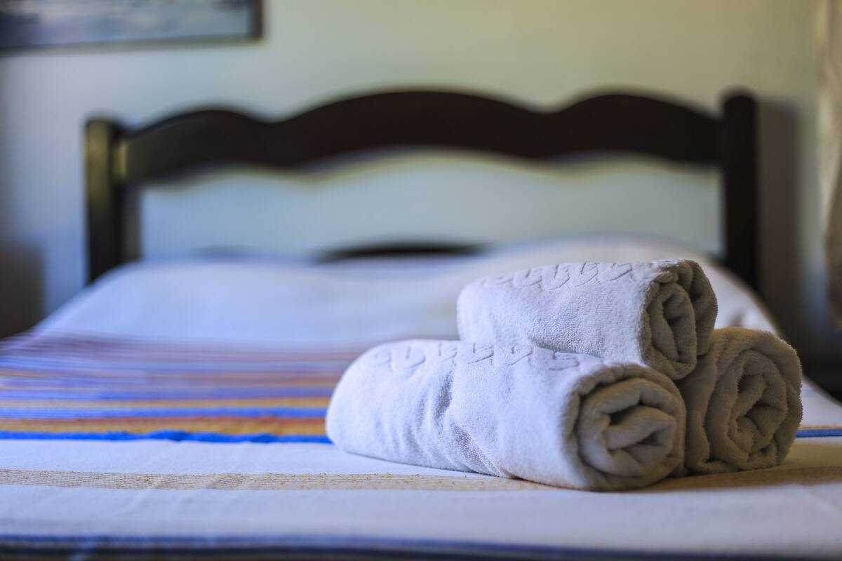 A neatly made bed with a striped bedspread and rolled towels.