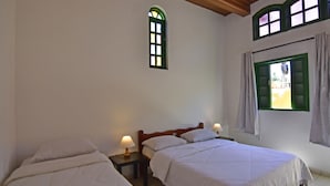 Un dormitorio con dos camas, una mesita y un ventanal con cortinas.
