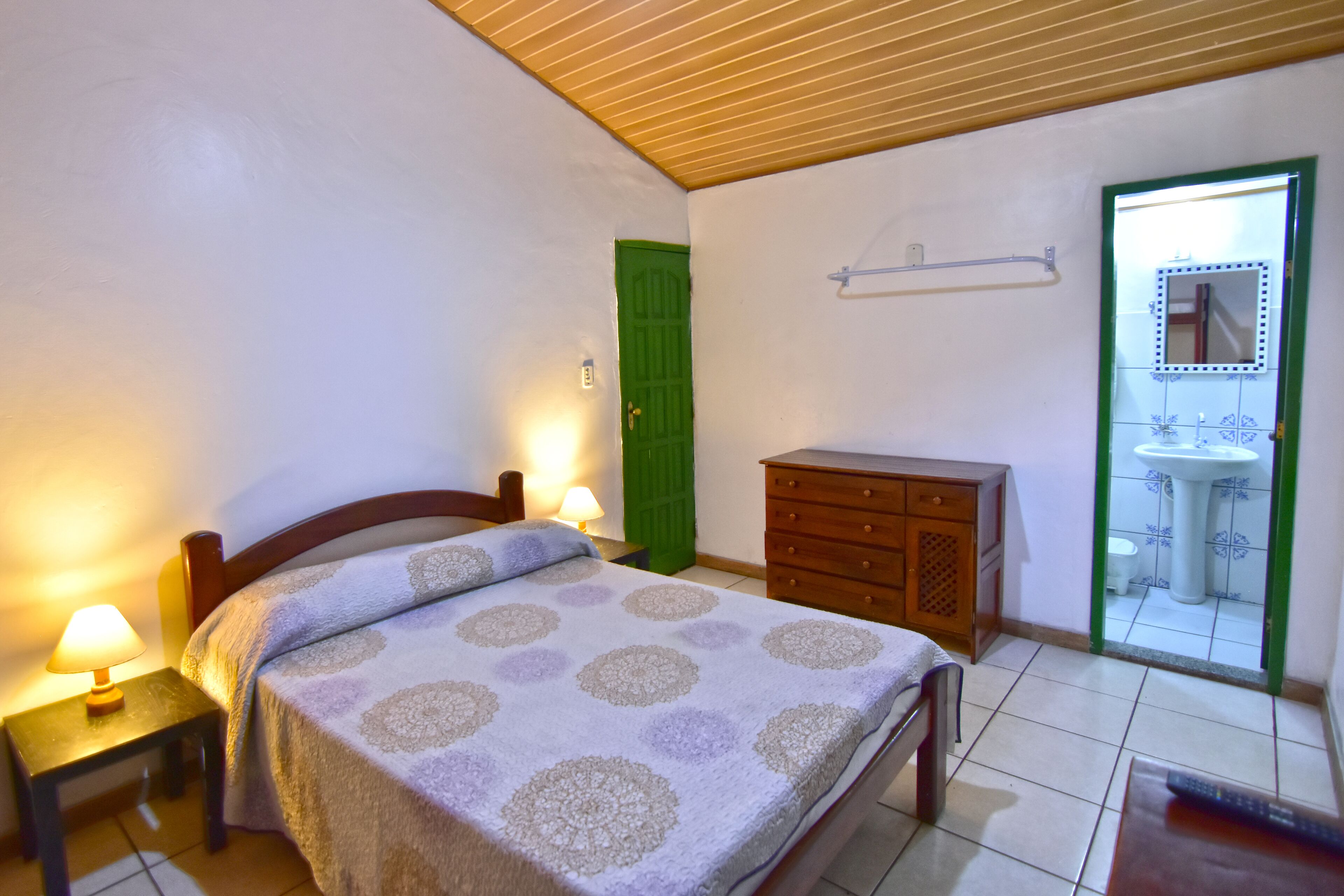 A bedroom with a bed, bedside lamps, a dresser, and a bathroom visible through an open door.