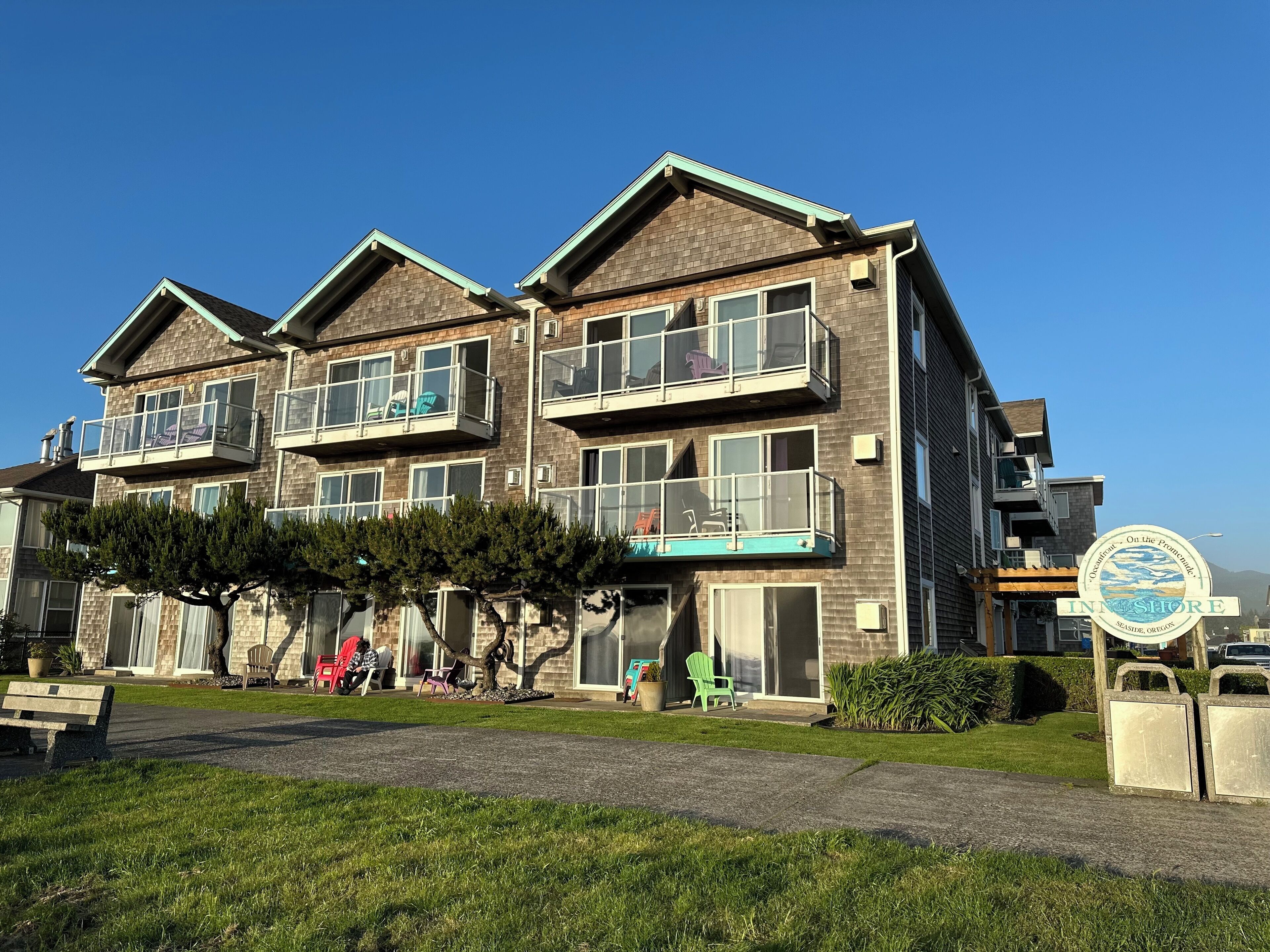 Un hotel de varios pisos con balcones, mobiliario exterior y un cartel que indica que se encuentra en Seaside, Oregon.