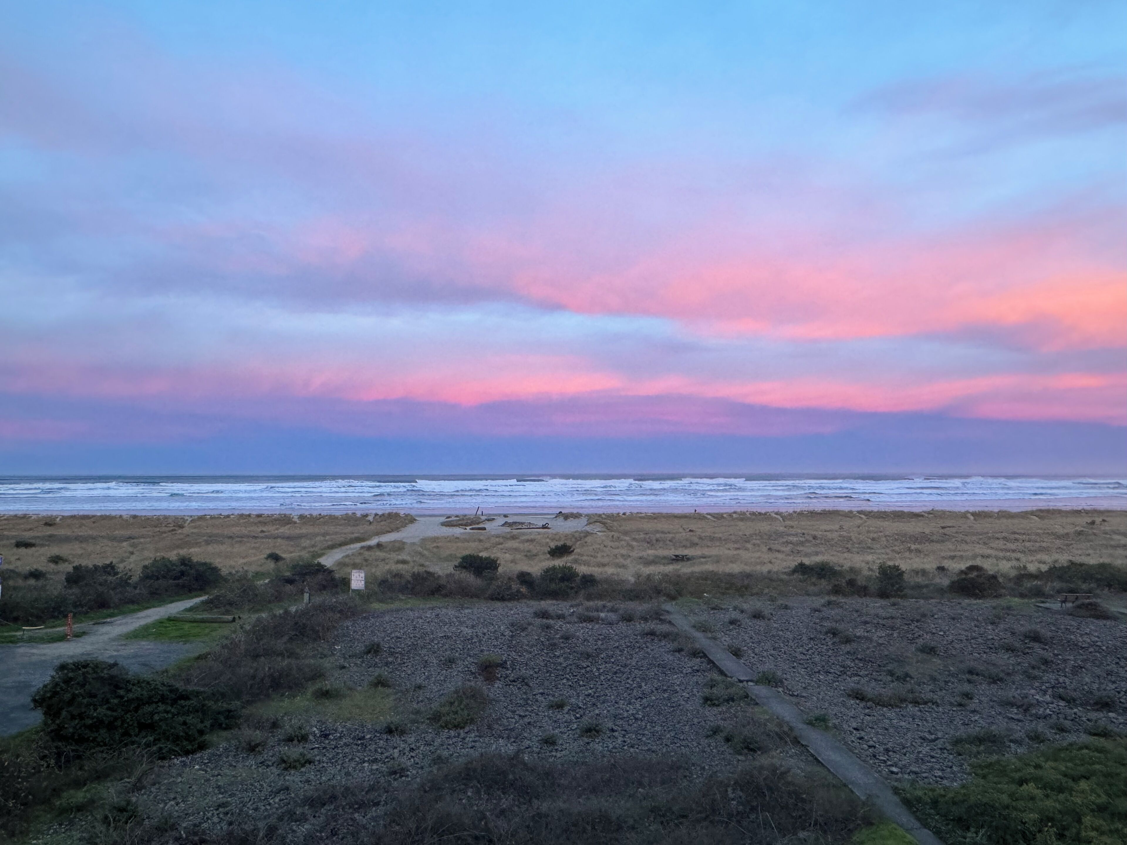 A coastal landscape with a path leading to the beach, under a colorful sky.