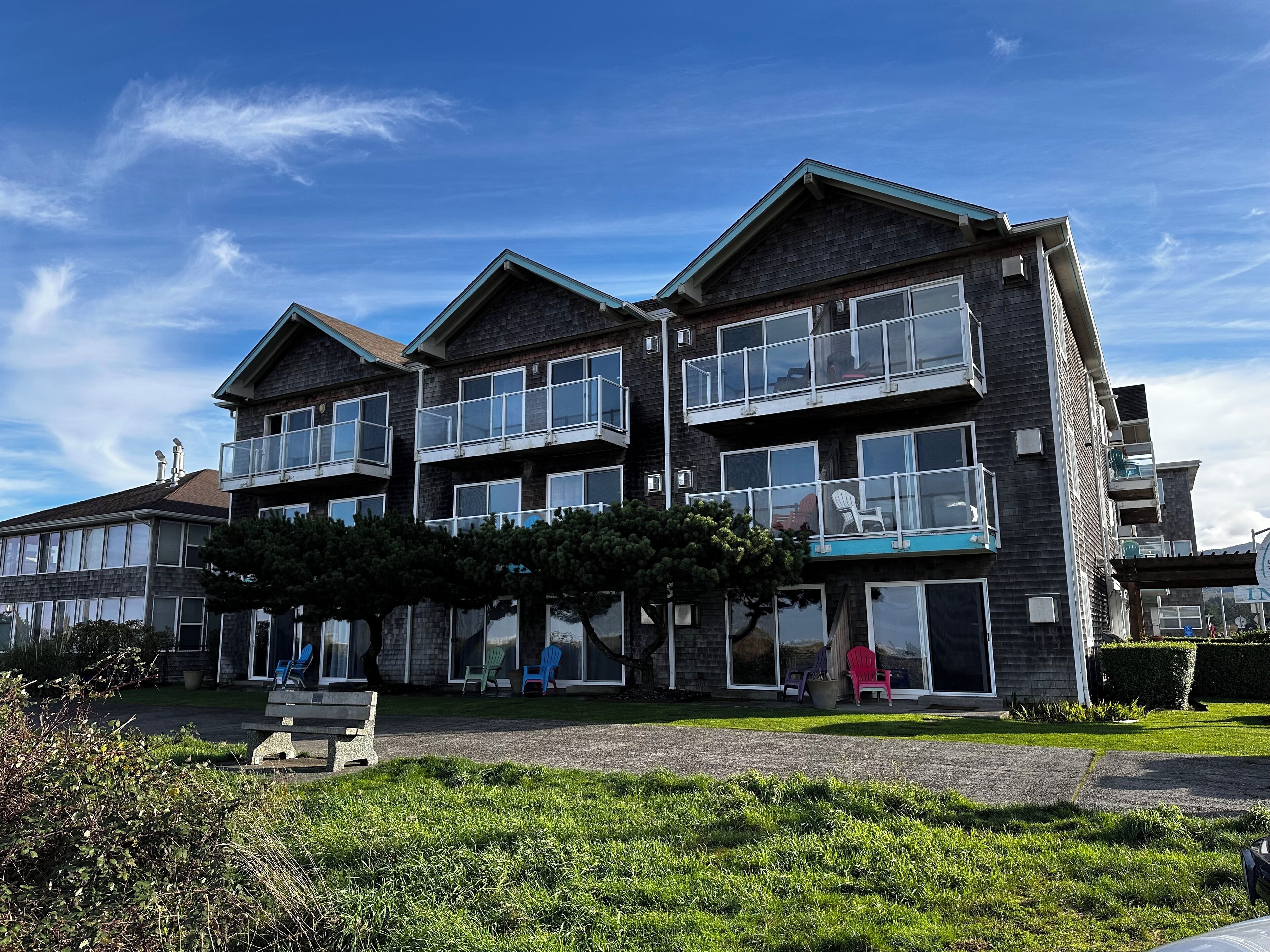 A multi-story building with large windows and balconies, a well-maintained lawn, and a clear sky.