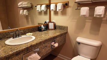 Une salle de bain dotée d’un comptoir en granit, d’un lavabo, de toilettes et de plusieurs porte-serviettes.