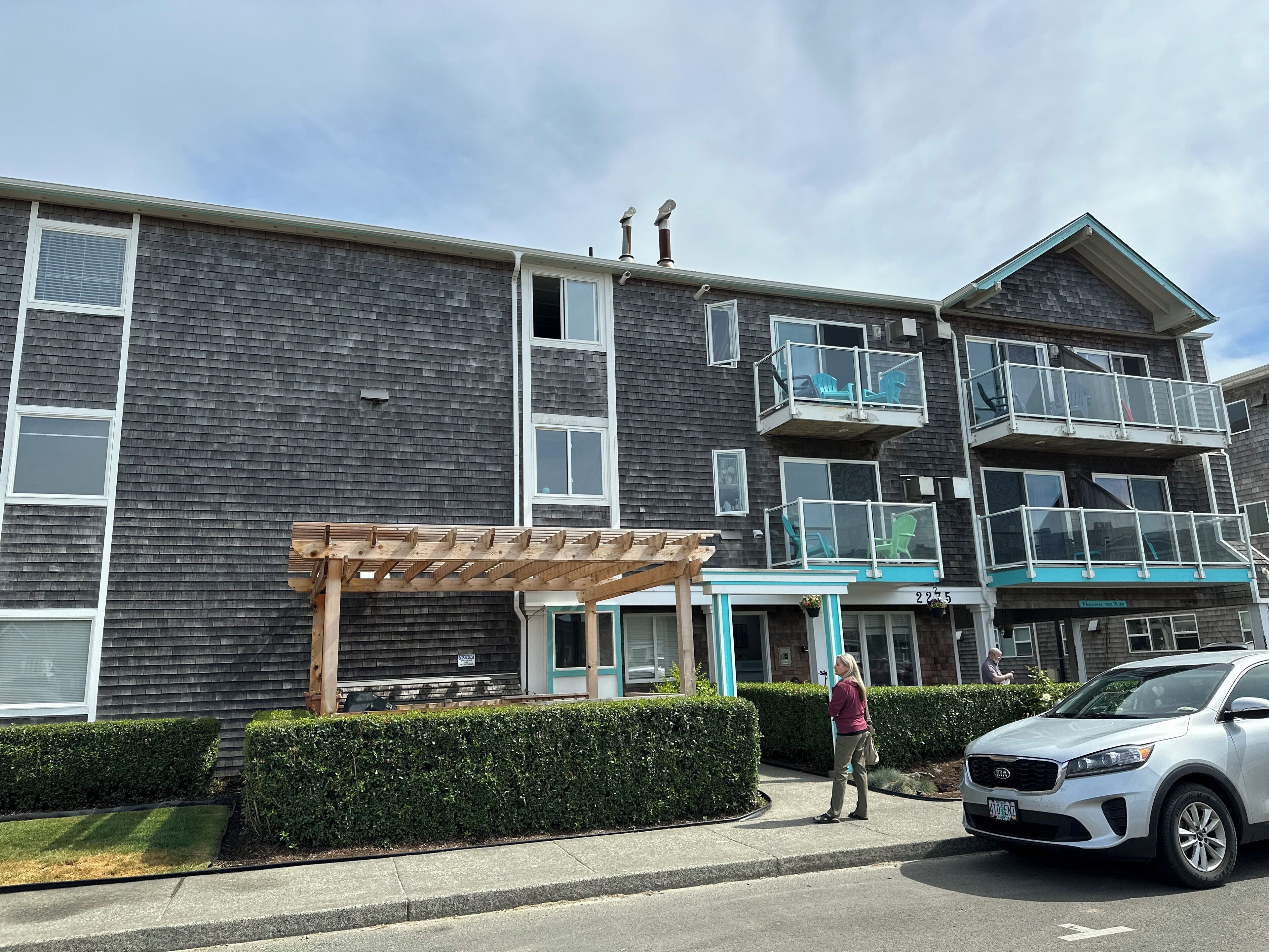 A multi-story building with balconies, a covered patio, and a parked car.
