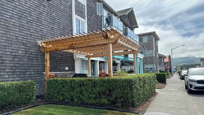A residential building with a wooden pergola, a well-maintained lawn, and a sidewalk with parked cars.