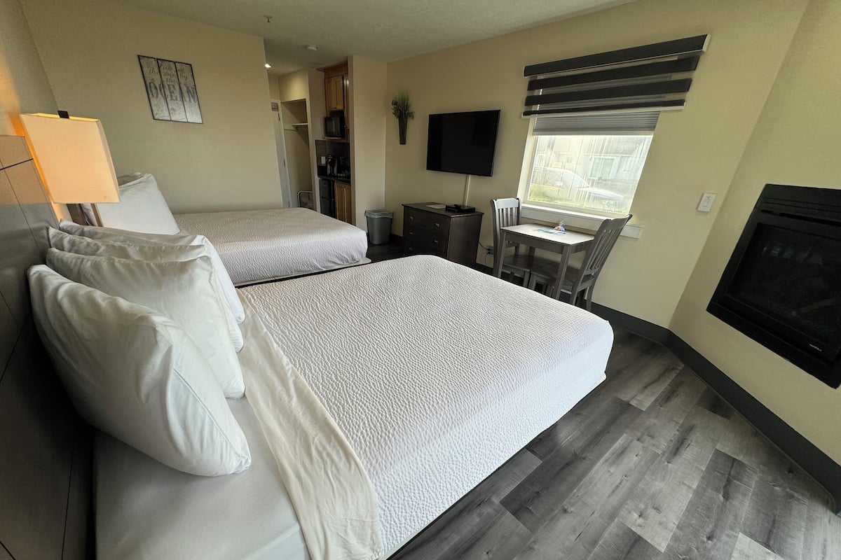 A hotel room with two beds, a desk, a TV, and a fireplace.