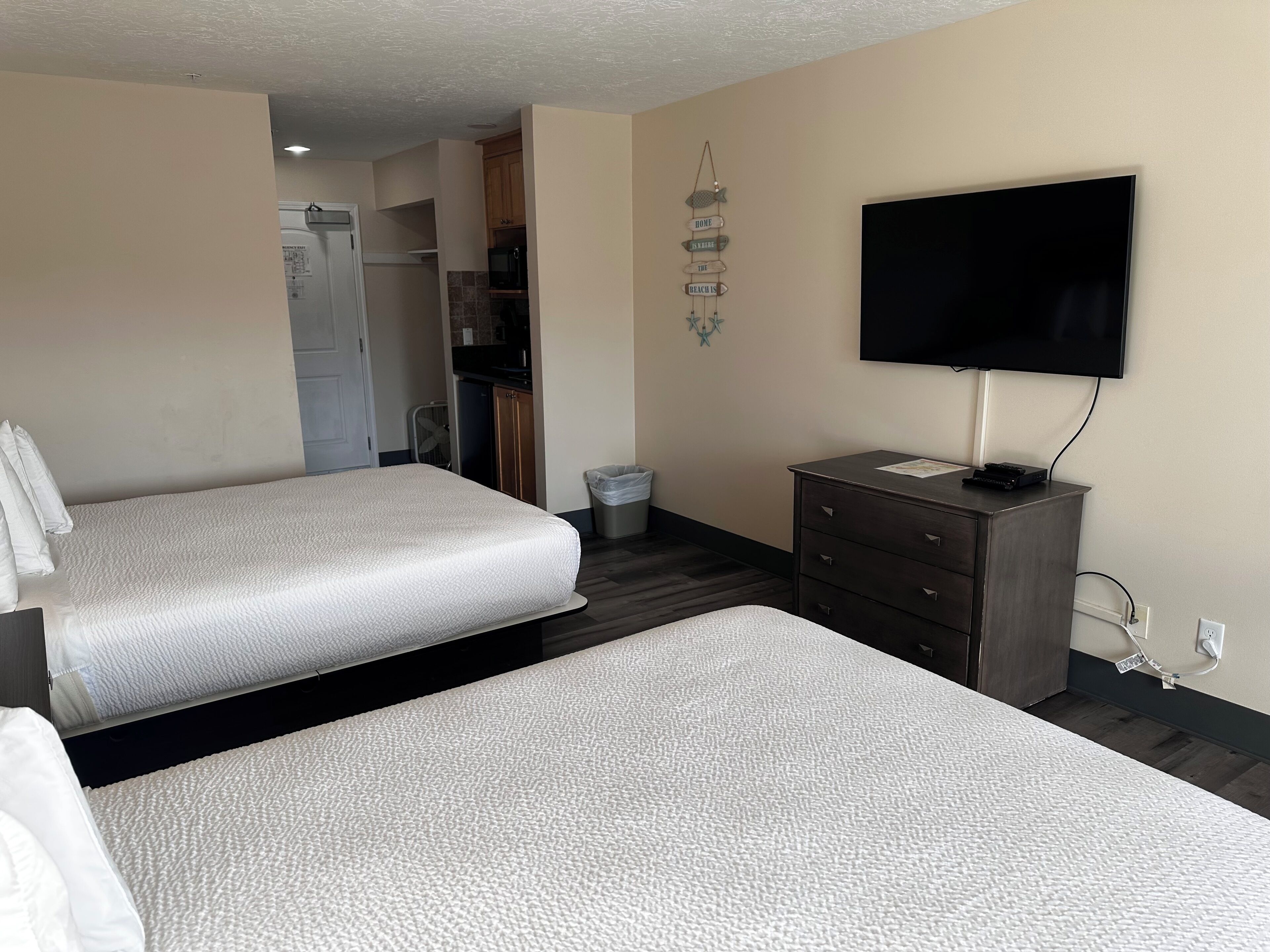 Ein Hotelzimmer mit zwei Betten, einem Fernseher, einem Schminktisch und einer Küchenzeile.