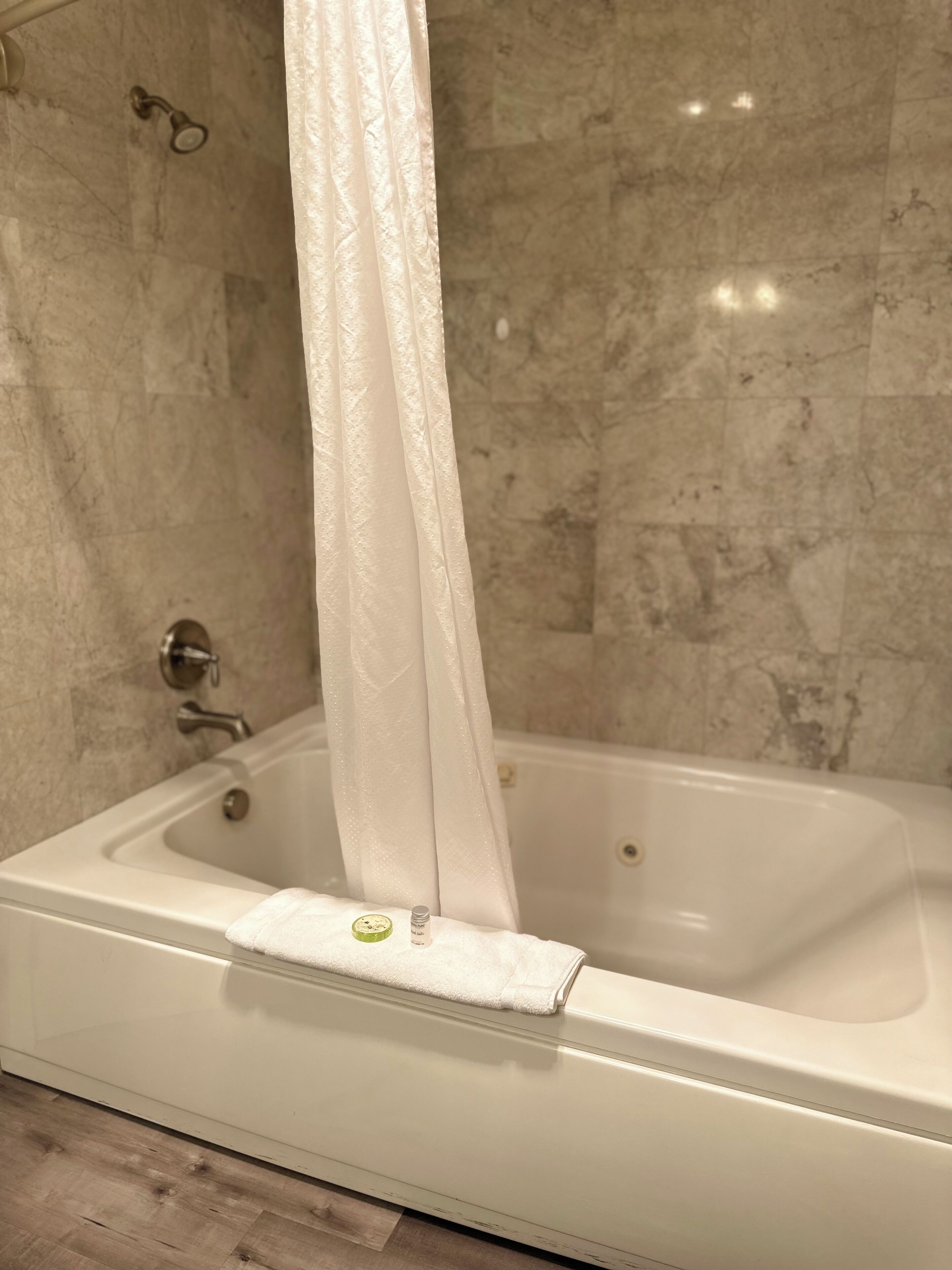 A bathtub with a shower curtain, a towel, and a bottle of lotion on the edge.