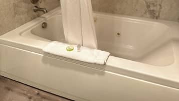 A bathtub with a shower curtain, a towel, and a bottle of lotion on the edge.