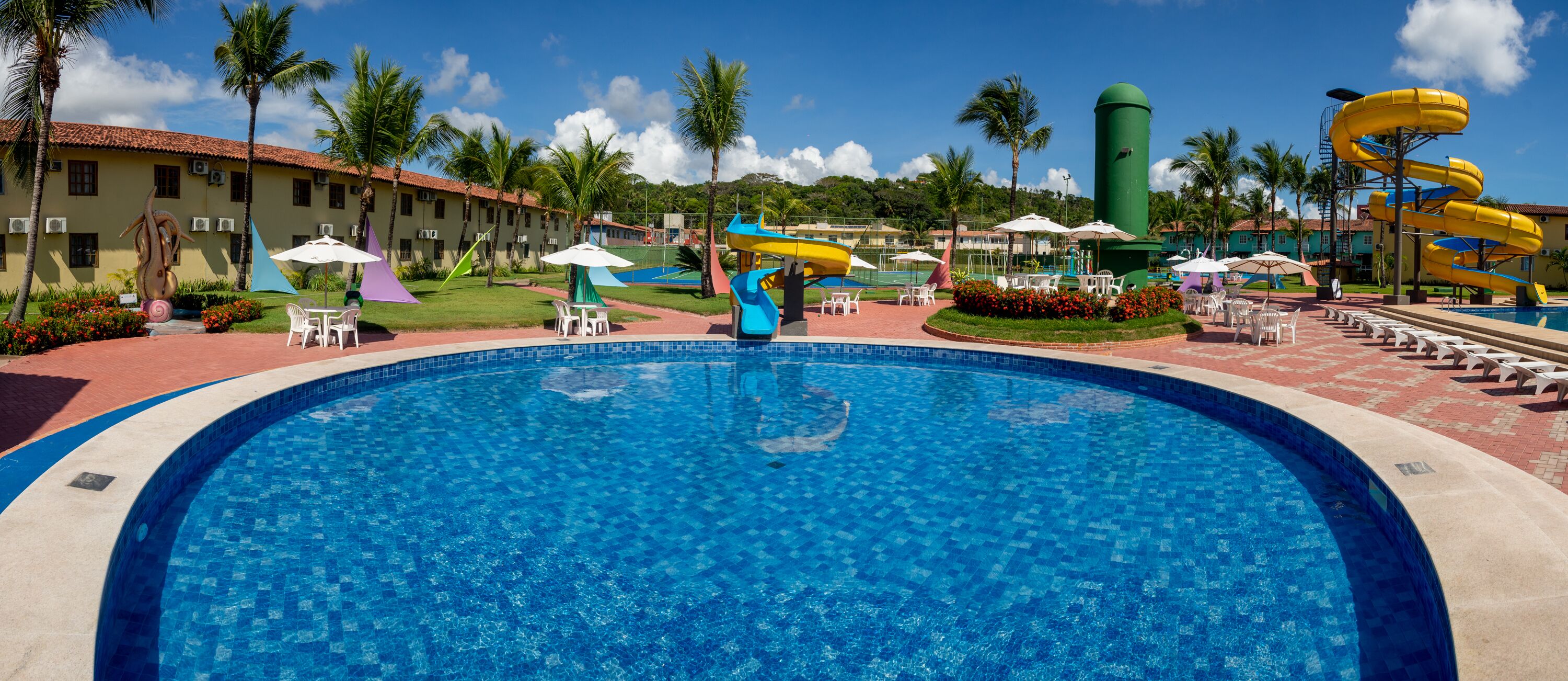 A swimming pool with a water slide, lounge chairs, and umbrellas.