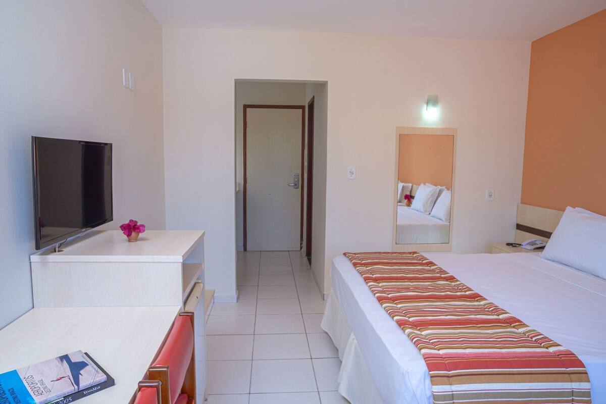 Una habitación de hotel con cama, televisión, escritorio y espejo.