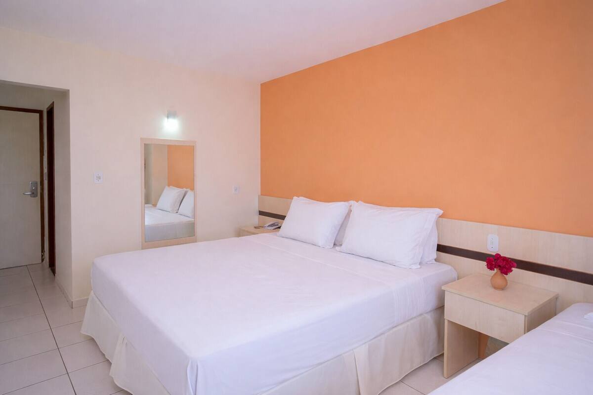 Una habitación de hotel con una cama grande, una mesita de noche, un espejo y un florero con flores.
