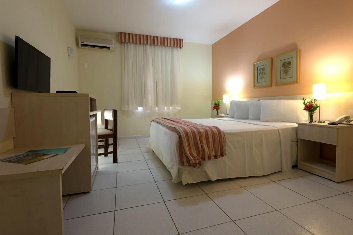 Een hotelkamer met een bed, nachtkastje, lamp en een bureau met stoel.