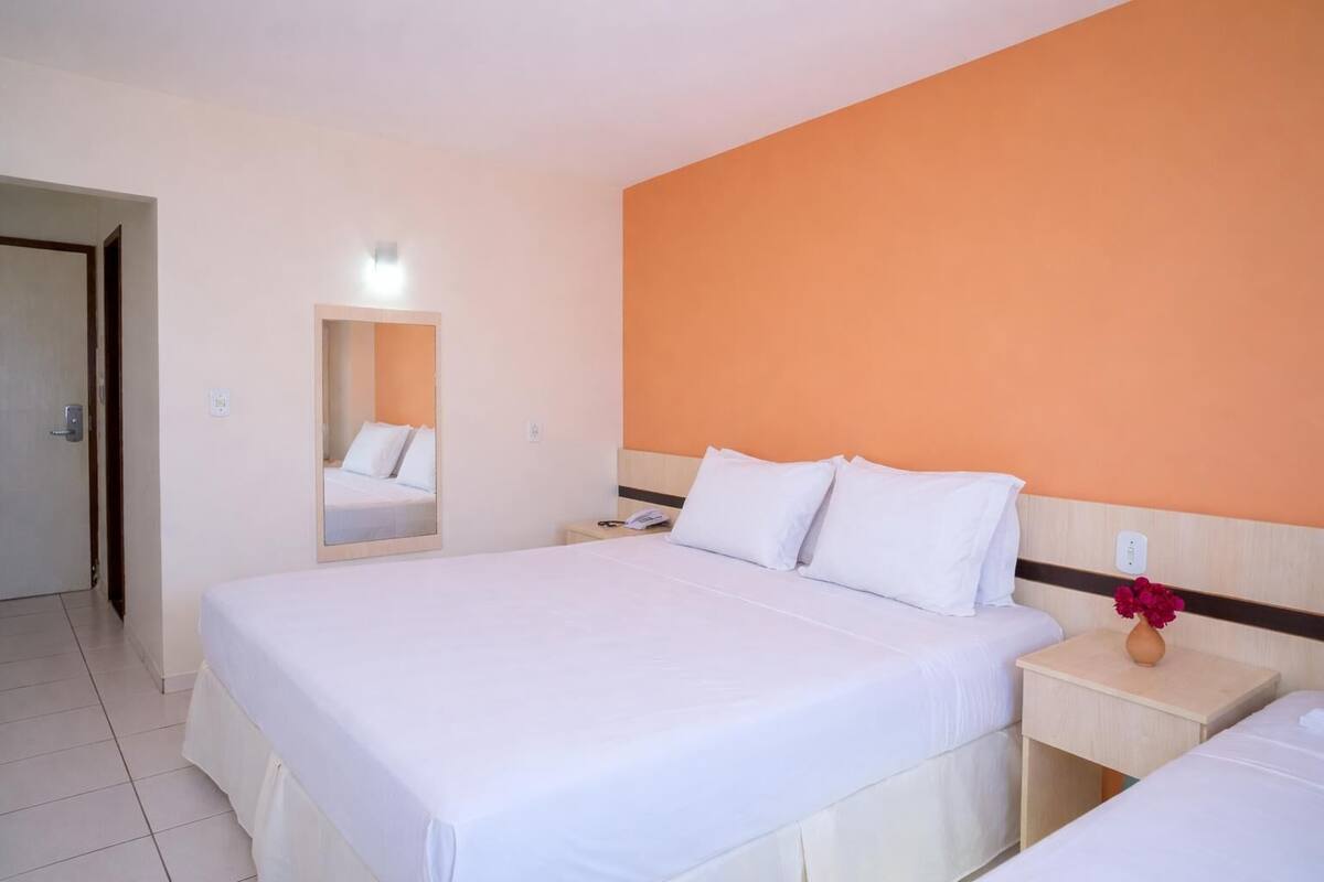 Una habitación de hotel con una cama grande, una mesita de noche con un teléfono, un espejo y un jarrón con flores.
