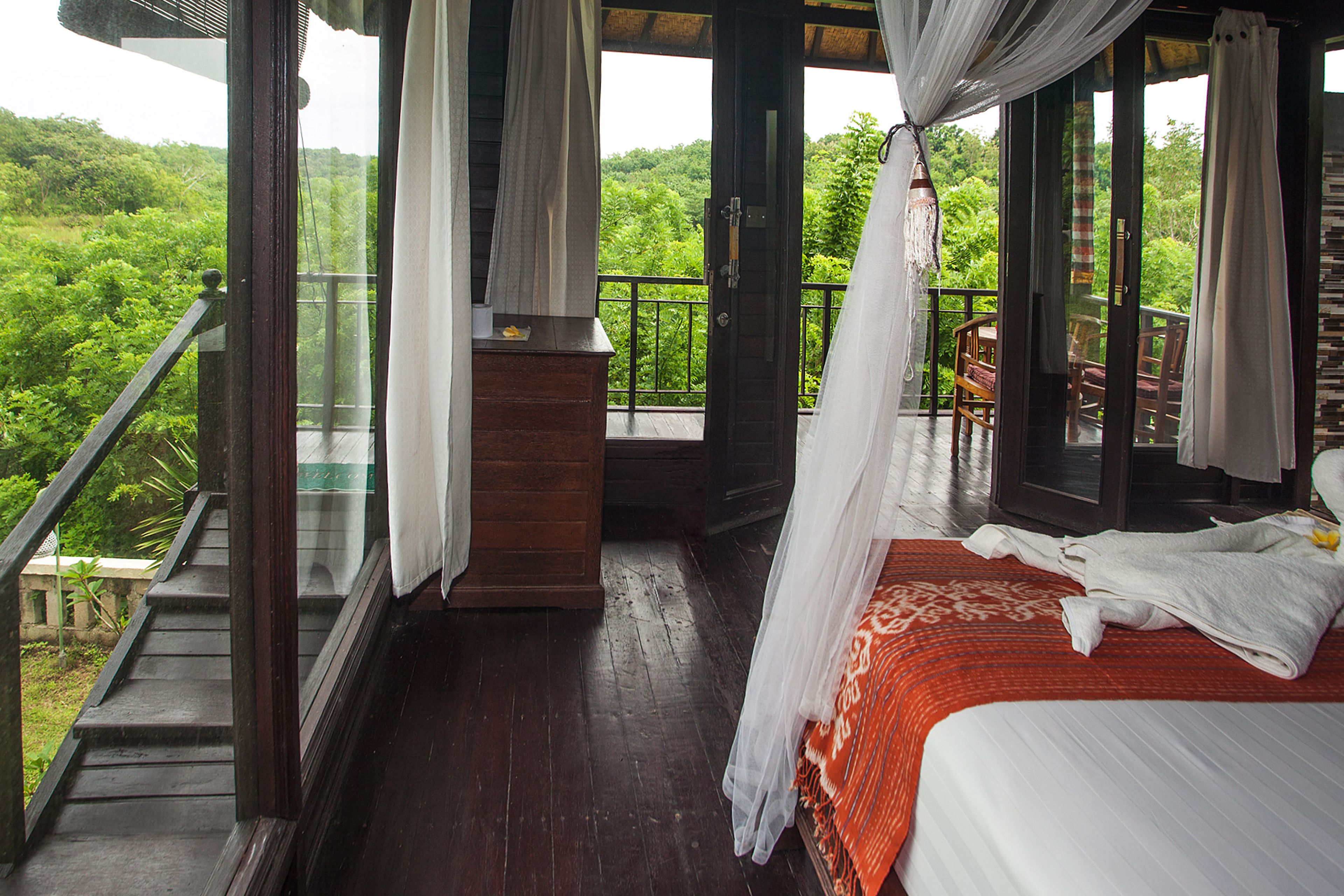 A room with a bed, a wooden dresser, and a balcony with a railing.