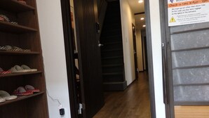Un pasillo con un zapatero de madera a la izquierda, una puerta que da a una escalera y un cartel en la pared derecha.