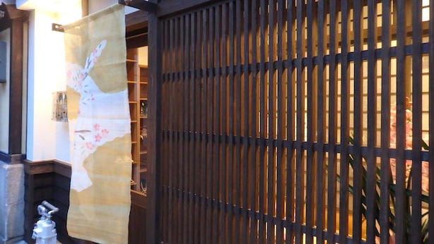 Un portón japonés tradicional con un biombo de papel corredizo, un pequeño elemento acuático y una estructura de madera a la izquierda.