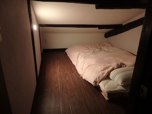Una stanza piccola e stretta con un letto a castello, pavimento in legno e una singola lampada a soffitto.