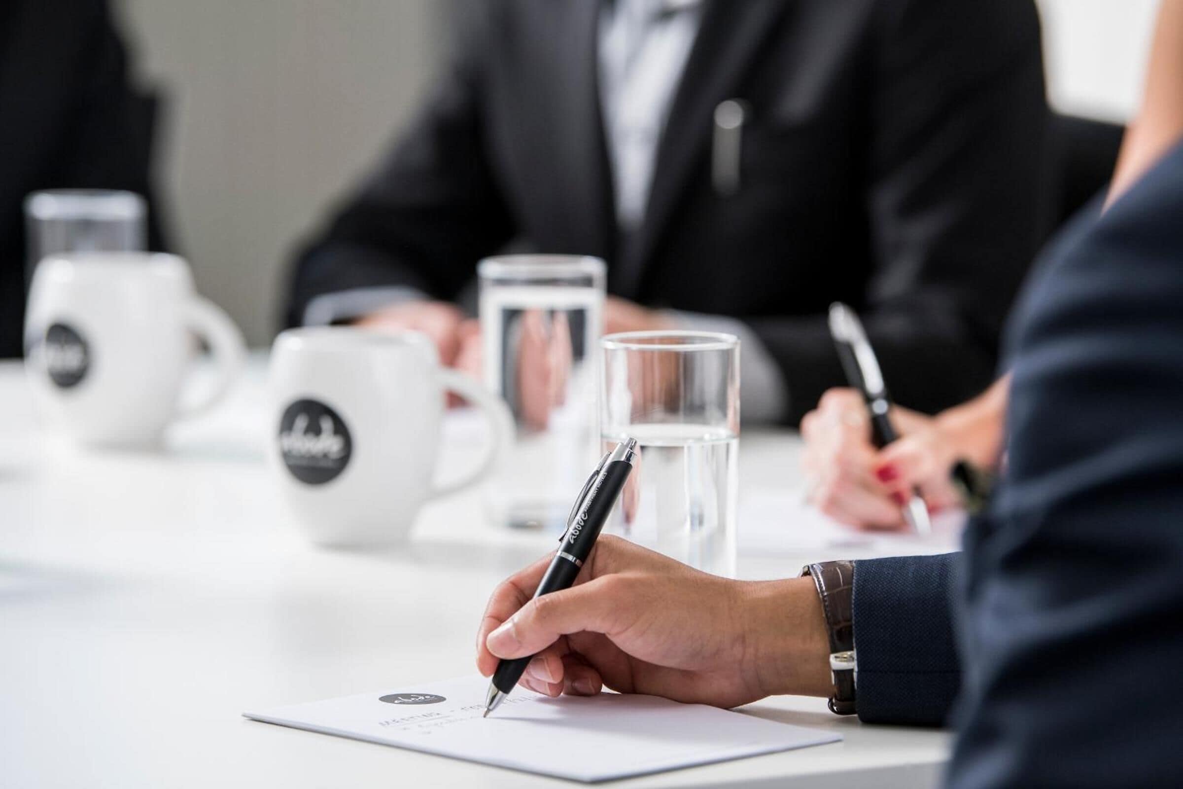 A meeting with participants seated around a table with documents, pens, and coffee mugs.