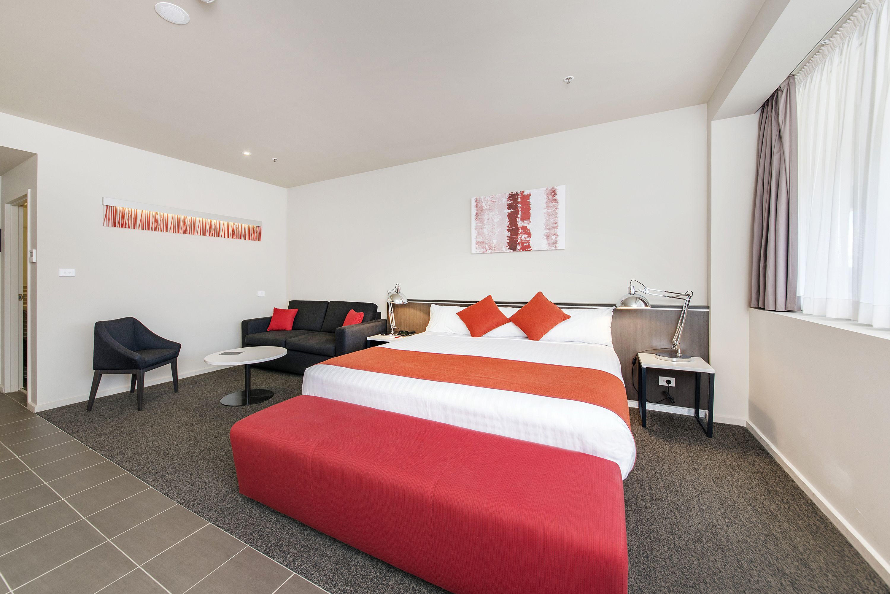 Ein Hotelzimmer mit einem großen Bett, einer Couch, einem Sessel, einem kleinen Tisch und einer Lampe.