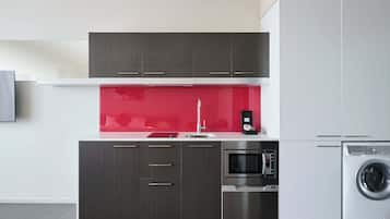 A modern kitchen with dark cabinets, a red backsplash, stainless steel appliances, and a built-in washing machine.