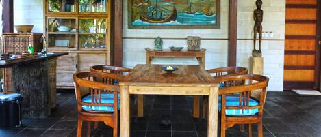 A wooden dining table with chairs, a bookshelf, a painting, and a statue in a room with tiled flooring.