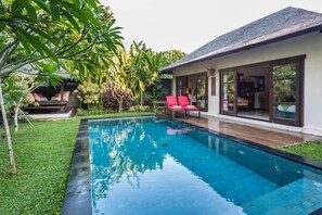 Une maison moderne avec une piscine, des chaises rouges et une végétation luxuriante.