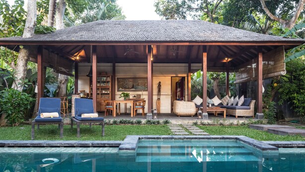 Un espacio al aire libre techado con piscina, sillones de descanso y zona de comedor.