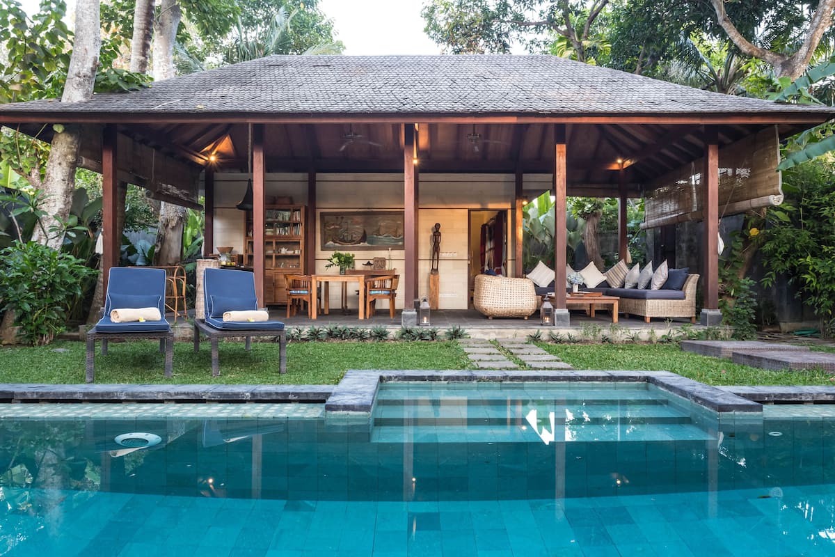 A covered outdoor area with a pool, lounge chairs, and a dining setup.