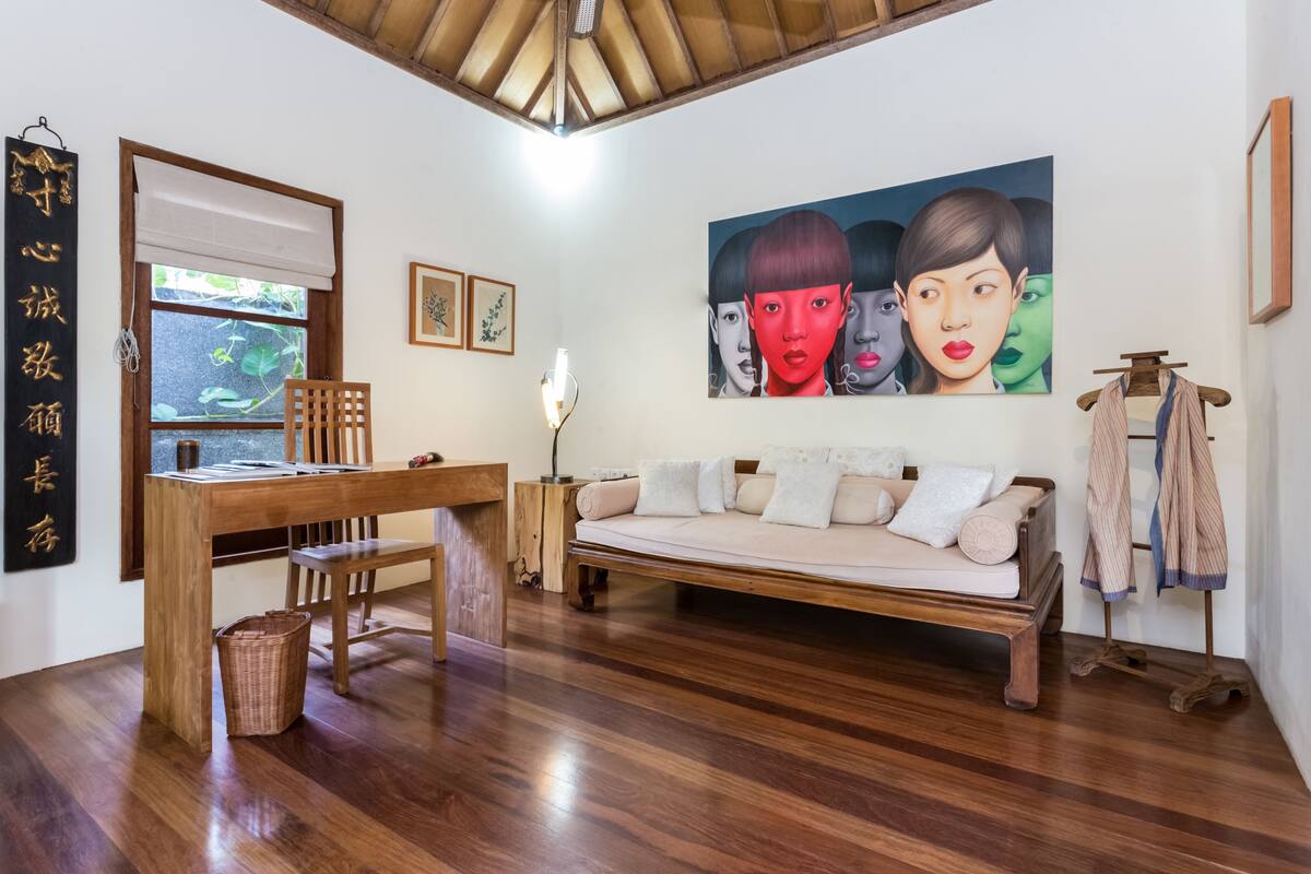 A room with a wooden desk, a sofa, a painting, and a clothing rack.