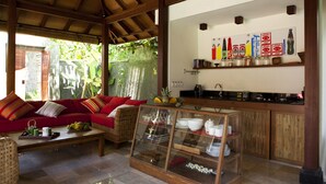 Una sala de estar acogedora con un sofá rojo, una vitrina de vidrio y una cocina con armarios de madera y un estante con diversos objetos.
