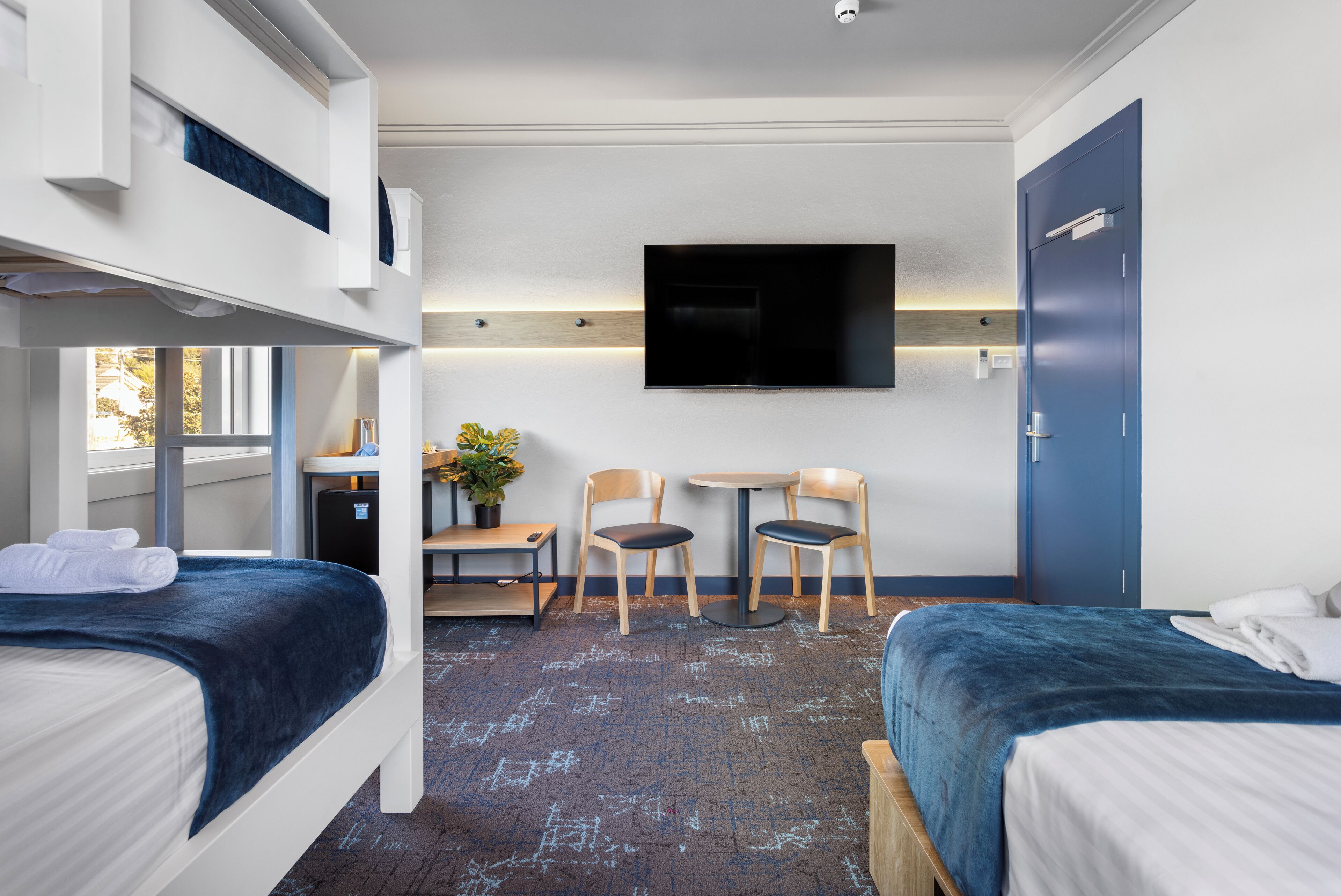 A hotel room with bunk beds, a desk, two chairs, a TV, and a wardrobe.