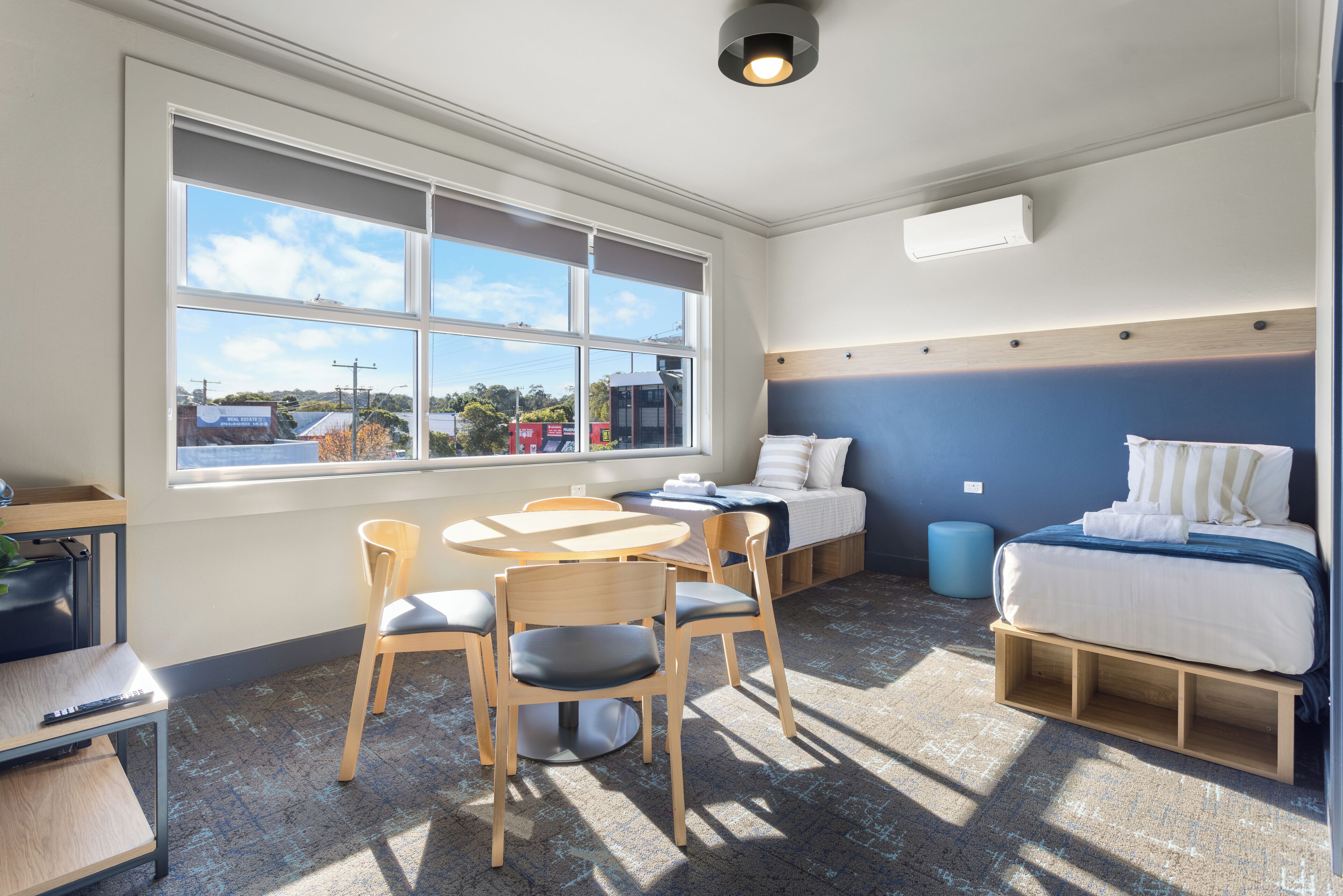 A compact room with a bed, a desk, and a chair. There is a window providing a view of the outside.