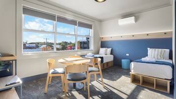 A compact room with a bed, a desk, and a chair. There is a window providing a view of the outside.
