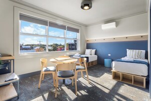 A compact room with a bed, a desk, and a chair. There is a window providing a view of the outside.
