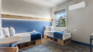 Een compacte hotelkamer met twee eenpersoonsbedden, een klein tafeltje en een raam met uitzicht op palmbomen.